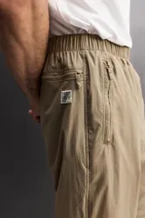 Pantalón jogger de corte regular confeccionado en tejido técnico ligero, con cintura elástica, bolsillos laterales con cierre y puños elásticos en los tobillos.