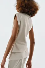 Top de algodón color beige con cuello recto, mangas asimétricas y detalle de tejido drapeado en el frente.