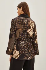 Saco tipo kimono con estampado batik en tonos marrones y negros, con solapas lisas, mangas largas y lazo ajustable en la cintura. Incluye bolsillos frontales y forro interior.