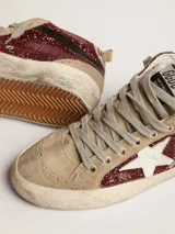 Zapatilla de caña media Golden Goose modelo Mid Star con upper cubierto de glitter color rojo oscuro/bordó. Presenta paneles en gamuza color beige claro y estrella lateral en cuero blanco. La suela tiene un efecto desgastado intencional.