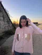 Camisa rosa de lana merino con bolsillos frontales con solapa dorada y cierre con botones. Corte recto y mangas largas.