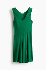 Vestido corto verde esmeralda sin mangas, con escote redondo y costura diagonal que define la cintura, creando una falda evasé.