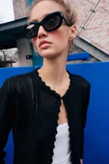 Chaqueta de punto calado con diseño pointelle, cuello redondo y manga larga. Presenta cierre frontal con corchete oculto y terminaciones con detalle de ondas en puños y ruedo.