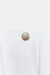 Camisa blanca de popelín, manga larga abullonada con puño ajustado y cuello redondo. Presenta frunces en el canesú delantero y trasero, creando un efecto holgado y corto.