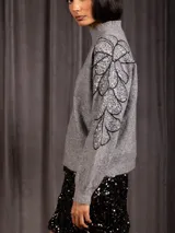 Buzo de cuello alto color gris, de manga larga, con detalle de bordado floral con lentejuelas en el hombro y parte superior de la manga.