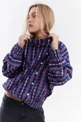 Chaqueta bomber de algodón con estampado a cuadros en tonos azules, amarillos y marrones, cuello alto y cierre frontal descentrado con botones. Cuenta con mangas abullonadas y puños elásticos.