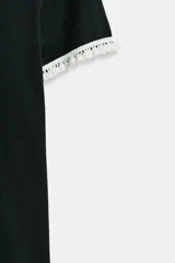 Camiseta de corte slim fit en color negro, con cuello redondo y manga corta. Presenta detalles de vivos en tejido de encaje blanco en el cuello y en los bordes de las mangas.