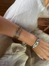 Pulsera rígida plateada hecha en alpaca, con diseño de líneas paralelas y otra pulsera rígida plateada con incrustaciones de piedras blancas.