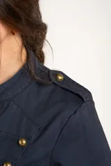 Chaqueta corta color beige de algodón, de inspiración militar con cuello mao y doble botonadura frontal con botones metálicos dorados.