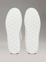 Zapatillas de corte bajo Calvin Klein, con diseño minimalista en color blanco y beige. Presentan una combinación de materiales en la capellada, incluyendo piel y ante, con detalles en contraste en el talón y logo de la marca en el lateral y la mediasuela.