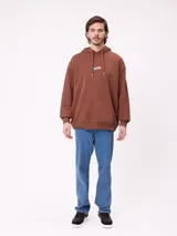 Canguro marrón con capucha y bolsillo frontal, con un diseño gráfico colorido en la espalda que representa una casa surrealista con el texto 'Supreal State of Mind'.