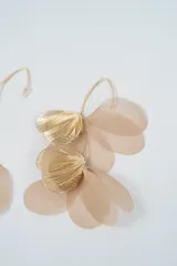 Caravanas colgantes con diseño de pétalos de tela en tono beige y detalles de hojas metálicas doradas con textura estriada.