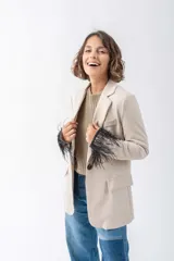 Blazer color beige con solapas de muesca, cierre frontal con un botón y bolsillos de parche. Las mangas largas están adornadas con plumas negras.