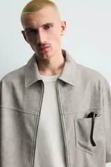 Sobrecamisa de manga corta efecto piel de corte relajado, color gris, con cuello solapa, bolsillo de parche en el pecho y cierre frontal con cremallera.