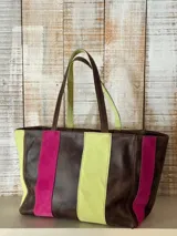 Bolso tipo shopper de cuero marrón, con tiras verticales decorativas de gamuza en colores verde lima y fucsia, asas dobles para el hombro y cierre superior.