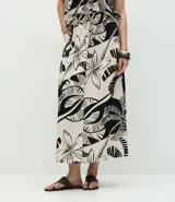Pollera larga (midi) de corte evasé, con cintura elástica y lazo. Presenta un estampado grande en blanco y negro de motivos tropicales como hojas de palmera y flores.