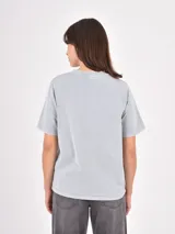 Remera de algodón color gris claro con efecto lavado, cuello redondo y detalle de pequeñas tachas metálicas dispersas en la parte superior delantera y mangas.