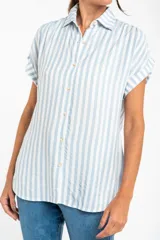 Camisa oversize celeste y blanca a rayas verticales, con cuello clásico, mangas cortas con dobladillo y cierre frontal con botones.