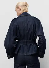 Abrigo corto estilo chaqueta de jean, confeccionado en algodón denim azul oscuro. Presenta cuello con solapas, cierre frontal, trabillas en los hombros y mangas largas con trabillas ajustables.