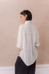 Camisa lila oversize de algodón con bordado floral calado tipo broderie, cuello camisero, manga larga y abotonadura frontal.