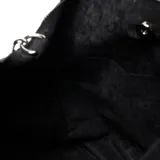 Cartera tipo tote bag de gamuza negra con detalles de tachas metálicas plateadas en los laterales y logo grabado en el centro. Cuenta con doble asa de mano y correa ajustable extraíble.