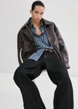 Camisa oversize de algodón estilo denim, de color azul con estampado de rayas, cuello camisero, manga larga con puños abotonados, bolsillo de parche en el pecho y cierre frontal con botones.