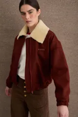 Campera bomber marrón de paño de lana, con cierre frontal, cuello de corderito sintético blanco desmontable, bolsillos laterales, puños y dobladillo elásticos, y logo bordado en el pecho.