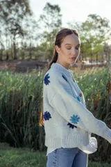 Cardigan de lana color celeste con cuello redondo, cierre frontal con botones color naranja y flores bordadas en azul y celeste.