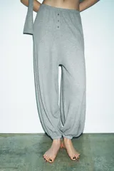 Pantalón de tiro alto confeccionado en tejido de punto mezcla de algodón, con cintura elástica y detalle de botones frontales. Presenta un diseño de pernera amplia con bajo abullonado acabado en elástico.