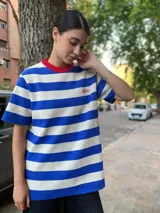 Remerón de mangas cortas con cuello redondo en color rojo y estampado a rayas horizontales azules y blancas. Presenta un pequeño bordado en el pecho.