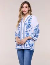 Blusa blanca con bordados florales en azul, de manga tres cuartos y cuello mao con escote en V.
