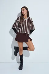 Remera de estilo deportivo con cuello en V y mangas cortas amplias. Presenta un diseño de rayas verticales en tonos marrones, blancos y líneas finas en fucsia, confeccionada en tejido de red.