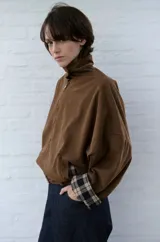 Campera de pana color marrón, con cuello alto y cierre frontal. Presenta un diseño holgado con mangas amplias y puños con detalle de forro a cuadros.