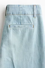 Jean de denim de algodón rígido color celeste claro, de tiro alto y corte recto holgado. Presenta bolsillos al bies y pliegues marcados adelante y atrás.