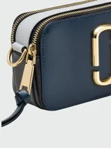 Cartera bandolera Marc Jacobs modelo The Snapshot, color azul con detalles dorados. Presenta doble compartimento con cierre, logo de la marca en el frente y correa de tela con el nombre de la marca.