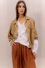 Campera liviana de lino color tostado, con cierre frontal de botones, bolsillos ojal en el pecho y mangas anchas con presilla y botón en los puños.