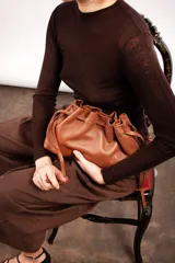 Bolso tipo sobre color bordó con diseño fruncido inspirado en la forma de un dumpling, con cierre ajustable mediante cordones y correa larga desmontable.
