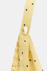 Top amarillo con lunares negros, cuello halter y escote fluido. Tiene un aplique metálico en el cuello y la espalda descubierta.