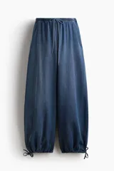 Pantalón tobillero de corte holgado en denim suave, de tiro bajo con elástico revestido en la cintura, cordón de ajuste y bolsillos laterales discretos. Presenta diseño de piernas globo con cordón ajustable fino en los bajos.