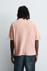 Camiseta de punto de algodón con corte boxy fit, cuello redondo y manga corta. Presenta un estampado frontal con diseño de paisaje y texto en tonos deslavados. La prenda tiene un efecto lavado que le da un aspecto envejecido e irregular.