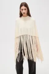 Poncho de punto color crudo con cuello alto y diseño de flecos largos en el ruedo.