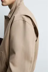 Cazadora de corte cropped confeccionada en tejido de algodón con interior ligeramente acolchado. Presenta cuello solapa, manga larga, bolsillos de vivo en la cadera y bajo ajustable con cordón. Cierre frontal mediante cremallera oculta por solapa con botones a presión.