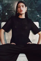 Top negro de manga corta en tejido de punto estilo crochet, con escote redondo, hombreras y cierre oculto en la espalda.