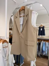 Chaleco sastrero color beige con solapas clásicas, bolsillos con solapa y cierre frontal con un botón.