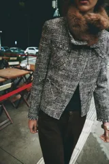 Chaqueta de tweed en tonos gris y negro, con cuello desmontable de pelo sintético marrón, bolsillos delanteros de plastrón y acabados deshilachados.