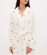 Bata de baño de corte regular confeccionada en tejido fleece de tacto suave y aspecto peludo. Presenta diseño de manga larga, abertura frontal con lazo ajustable en la cintura y bolsillos laterales. Cuenta con un estampado integral de cerezas sobre fondo blanco.