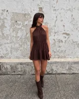 Vestido corto marrón con cuello halter fruncido, sin mangas, con elástico en la cintura y falda con volados escalonados.