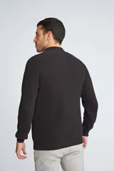 Sweater de tejido de punto acanalado en color negro, con cuello alto y cierre frontal parcial. Cuenta con mangas largas y un pequeño logo bordado en el ruedo.