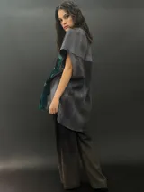 Poncho de lana merino afieltrada con cuello alto y mangas cortas. Diseño tipo mosaico con piezas geométricas en tonos verde azulado y gris.