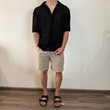 Camisa de manga corta con textura calada y tejido abierto, color negro, con cuello solapa y cierre frontal de botones.
